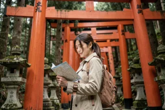 Voyageuse consultant une carte devant les torii rouges du sanctuaire Fushimi Inari à Kyoto, Japon